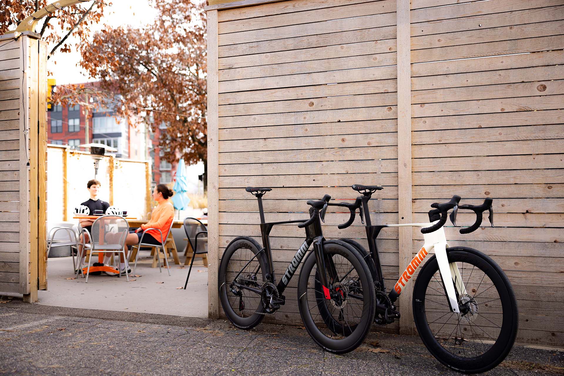 Two Stromm road bikes lean against an outdoor patio wall while the riders enjoy lunch on a bright sunny day.
