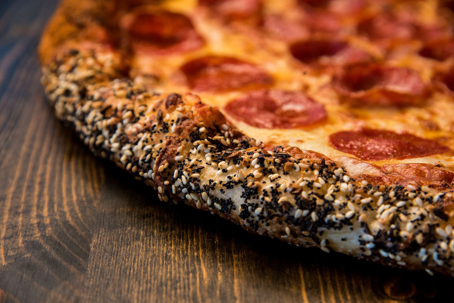 A close-up of the sesame seed encrusted crust of a pepperoni pizza.