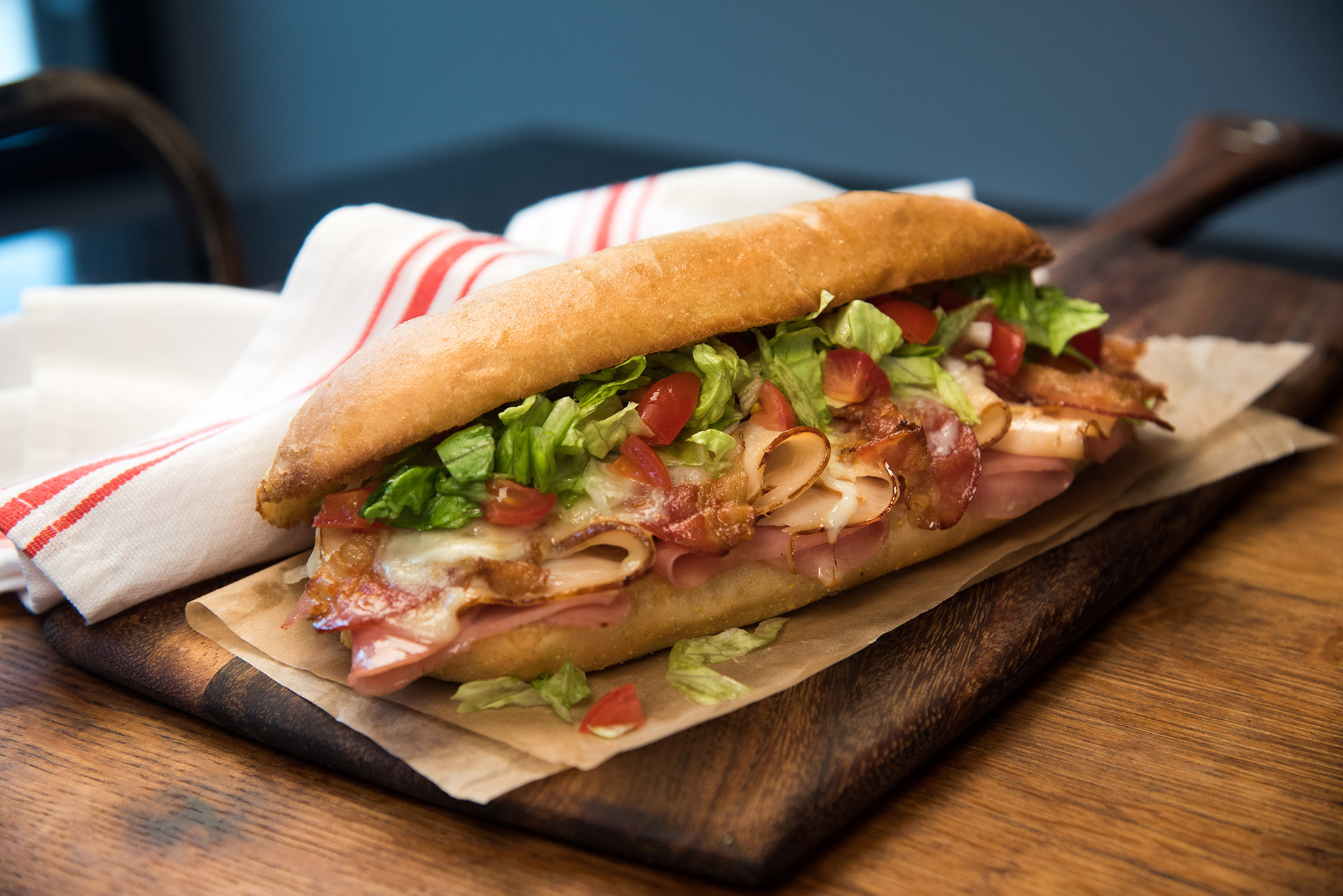 A club sub sandwich presented on a wooden paddle.